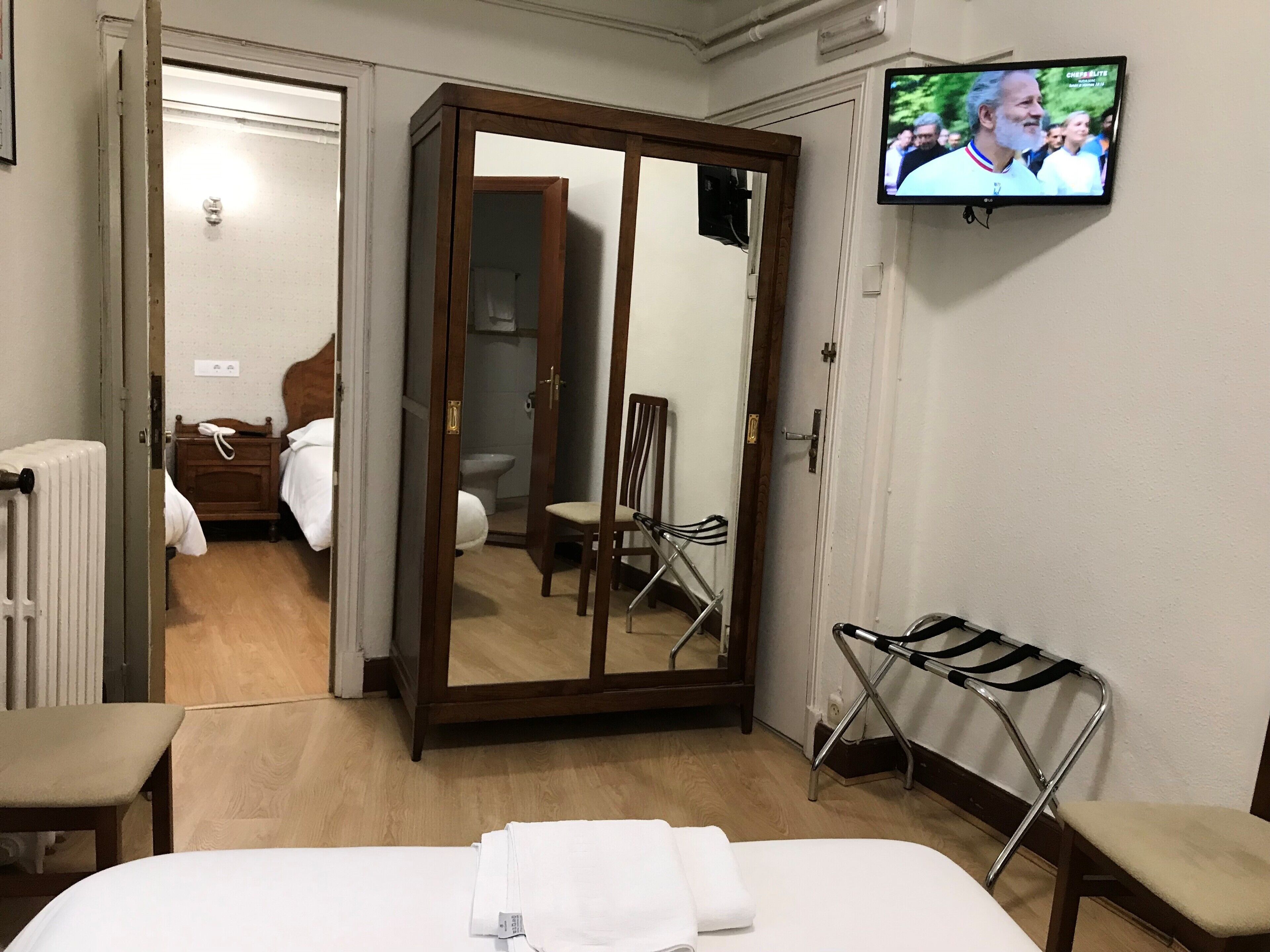 Habitación de hotel con cama, armario de madera, televisor y baño visible a través de una puerta abierta.