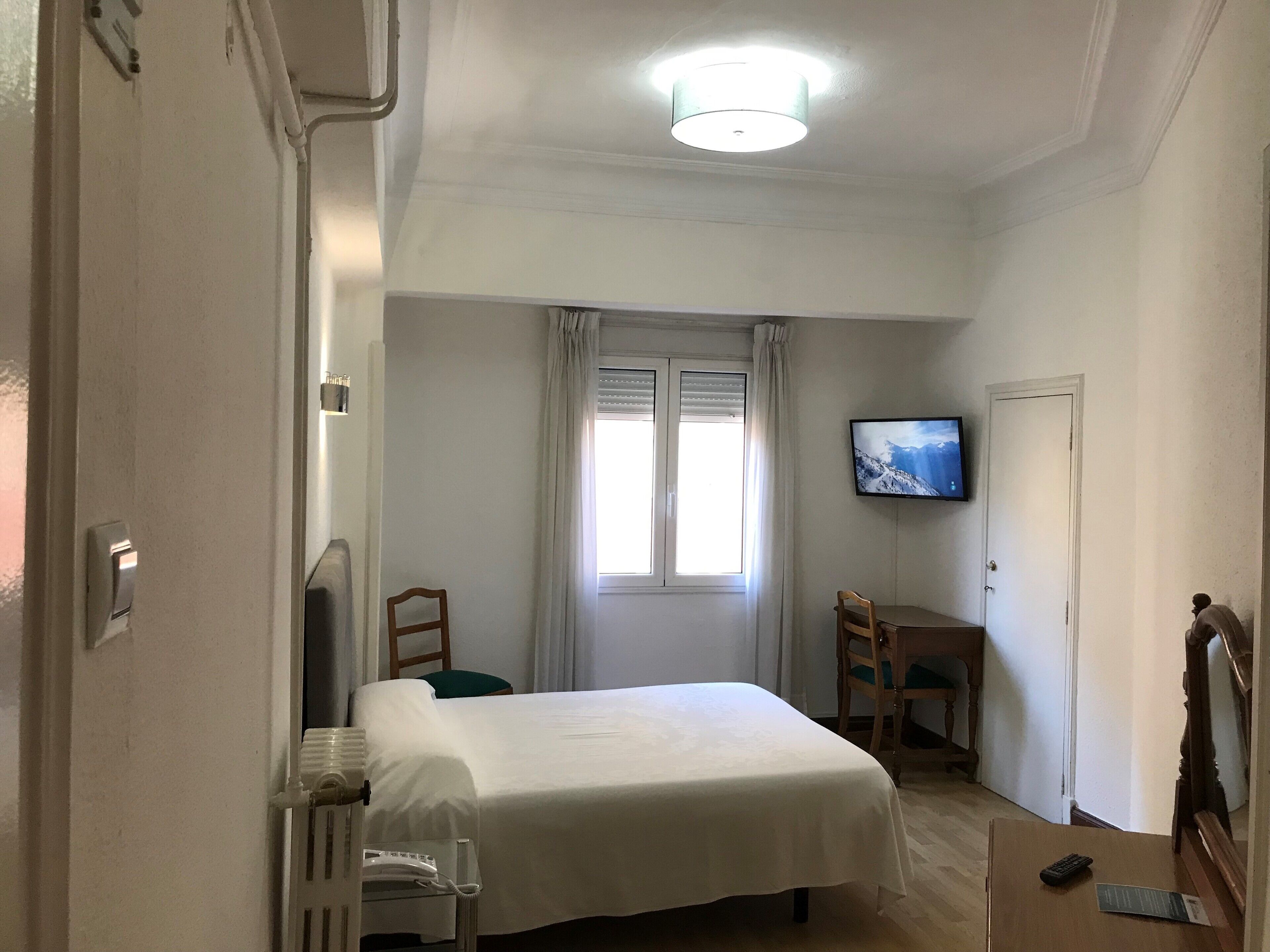 Habitació d'hotel amb un llit, escriptori, cadira, televisió i finestra amb cortines.