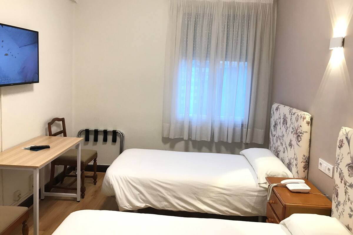 A hotel room with two beds, a desk, a chair, a TV, and a window with curtains.