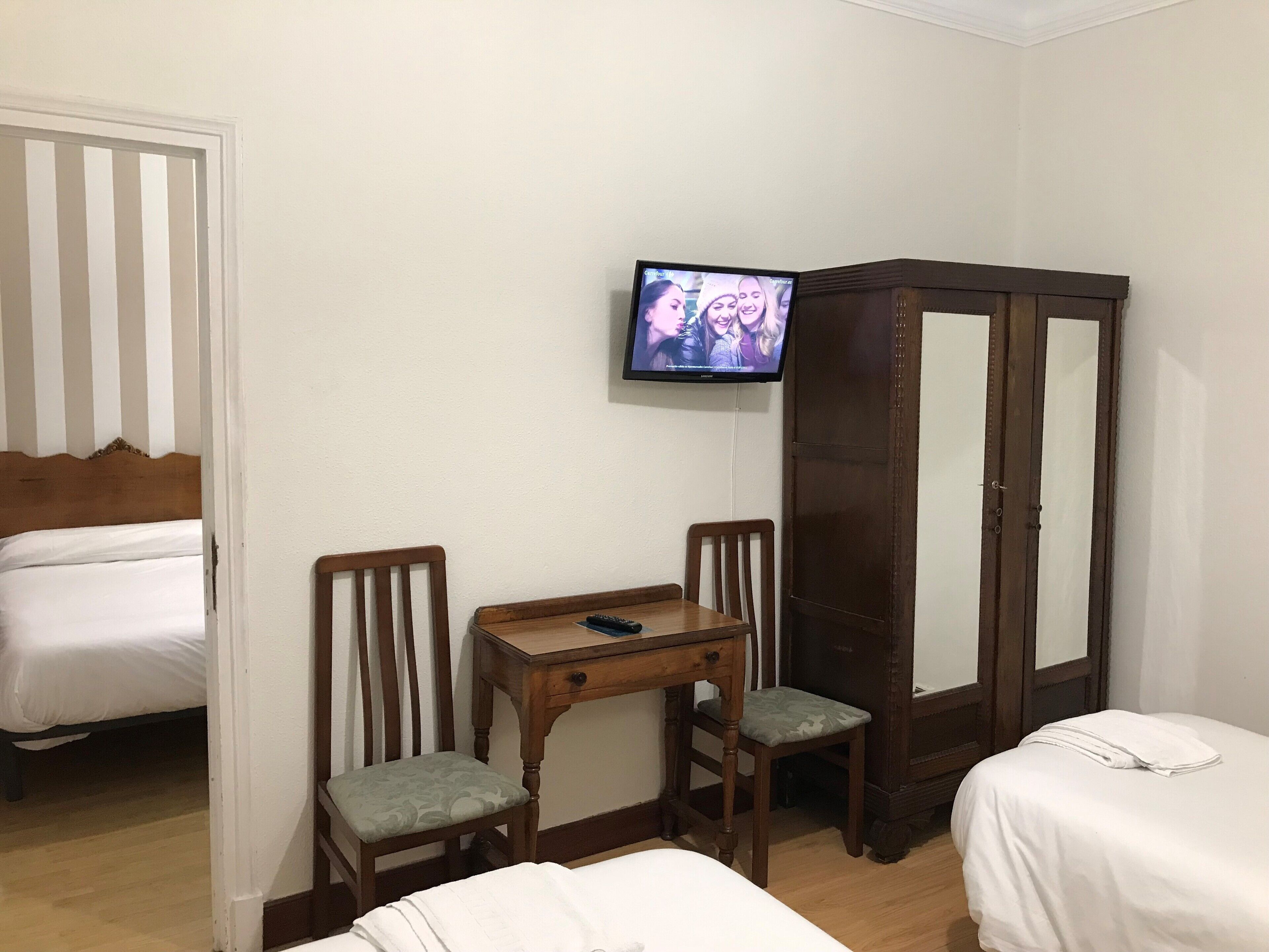 Habitación de hotel con dos camas, un armario de madera, una mesita con un mando a distancia y un televisor en la pared.