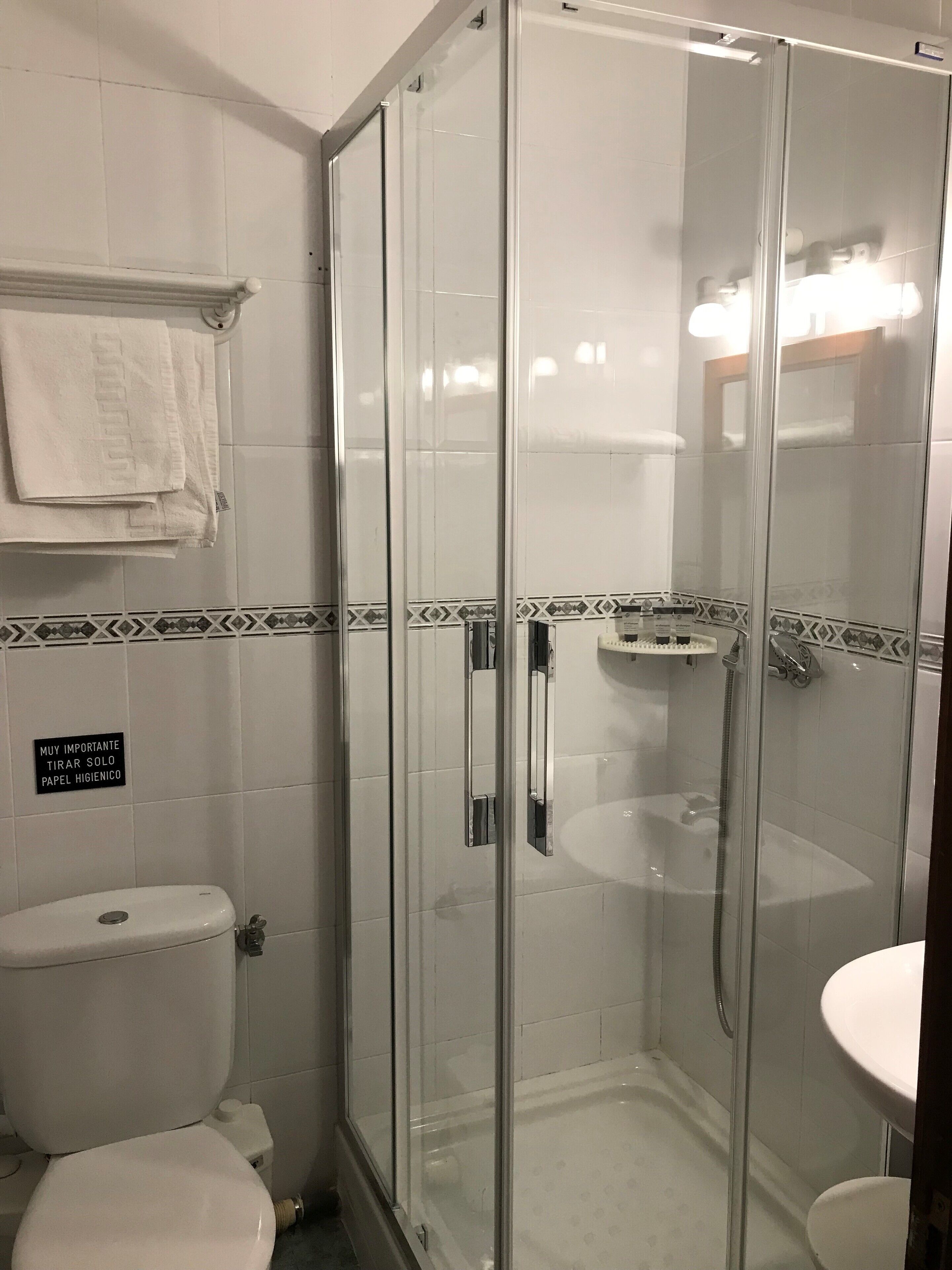 Cabina de ducha con paredes de vidrio, inodoro y lavamanos en un baño.