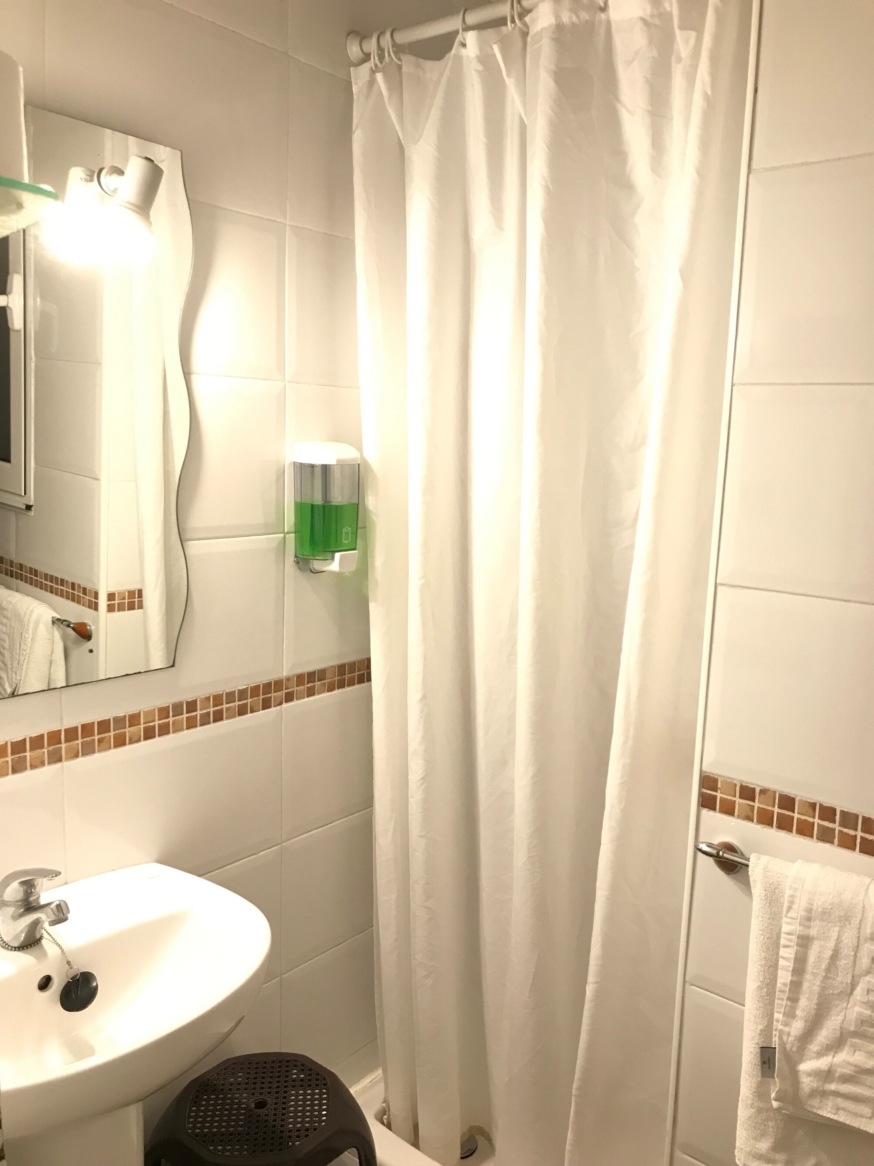Un baño con un lavabo blanco, un espejo, una cortina de ducha y un perchero para toallas.