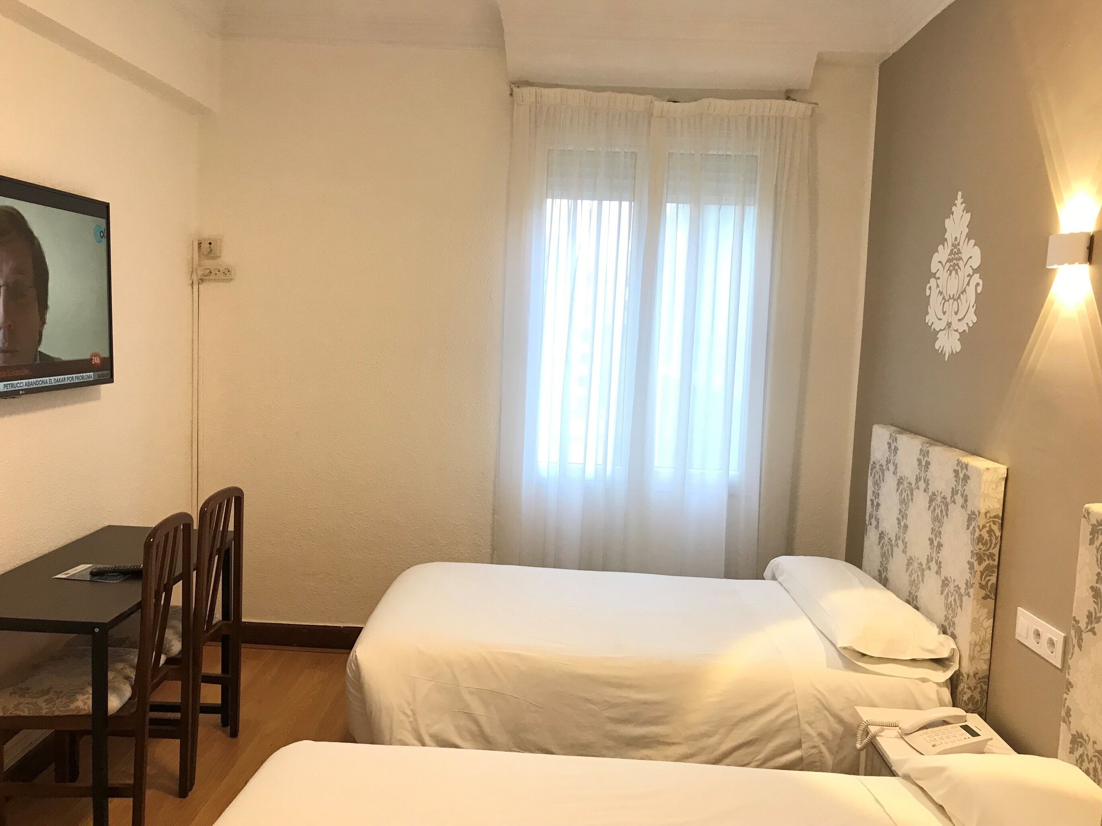 A hotel room with two beds, a desk, and a television.