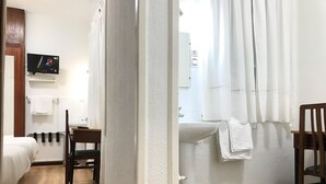 A hotel room with two beds, a wooden chair, a TV mounted on the wall, and a bathroom with a sink and toilet. - Hostal La Mexicana (Santander)