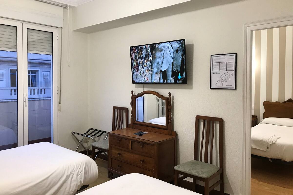 A hotel room with two beds, a wooden dresser, a chair, a television mounted on the wall, and a framed map.