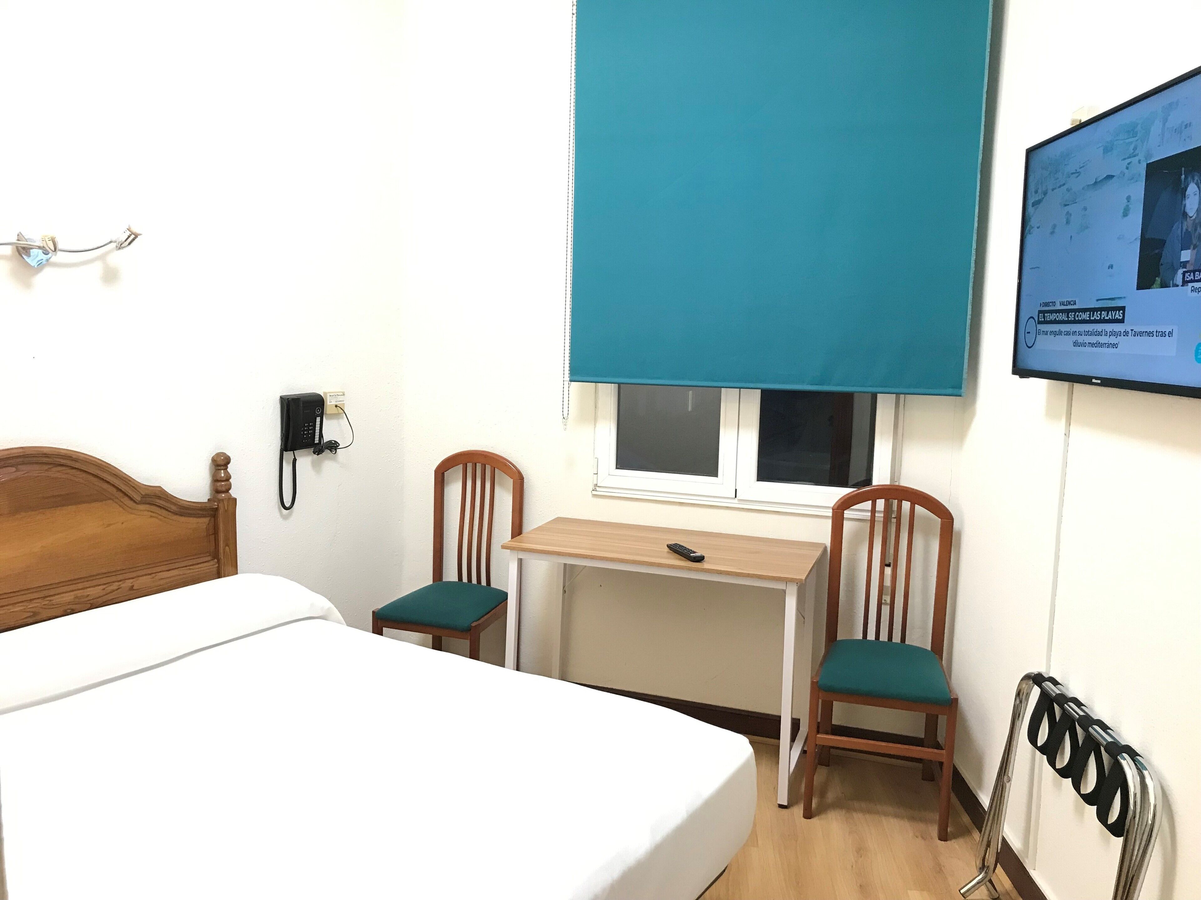 A hotel room with a bed, a desk, two chairs, a TV, and a window.