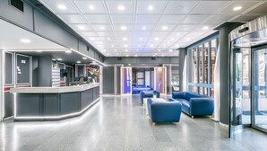 A modern lobby with a reception desk, seating area, and large windows. - Hotel Sansi Park (Lleida)