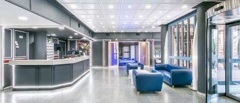 A modern lobby with a reception desk, seating area, and large windows.