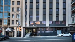 A modern hotel with a flat facade, large windows, and a visible entrance with a staircase leading to the lobby. - Hotel Sansi Park (Lleida)