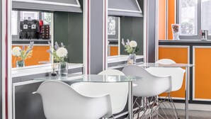 A modern dining area with a glass table and white chairs, a coffee machine, and decorative vases with flowers. - Hotel Sansi Park (Lleida)