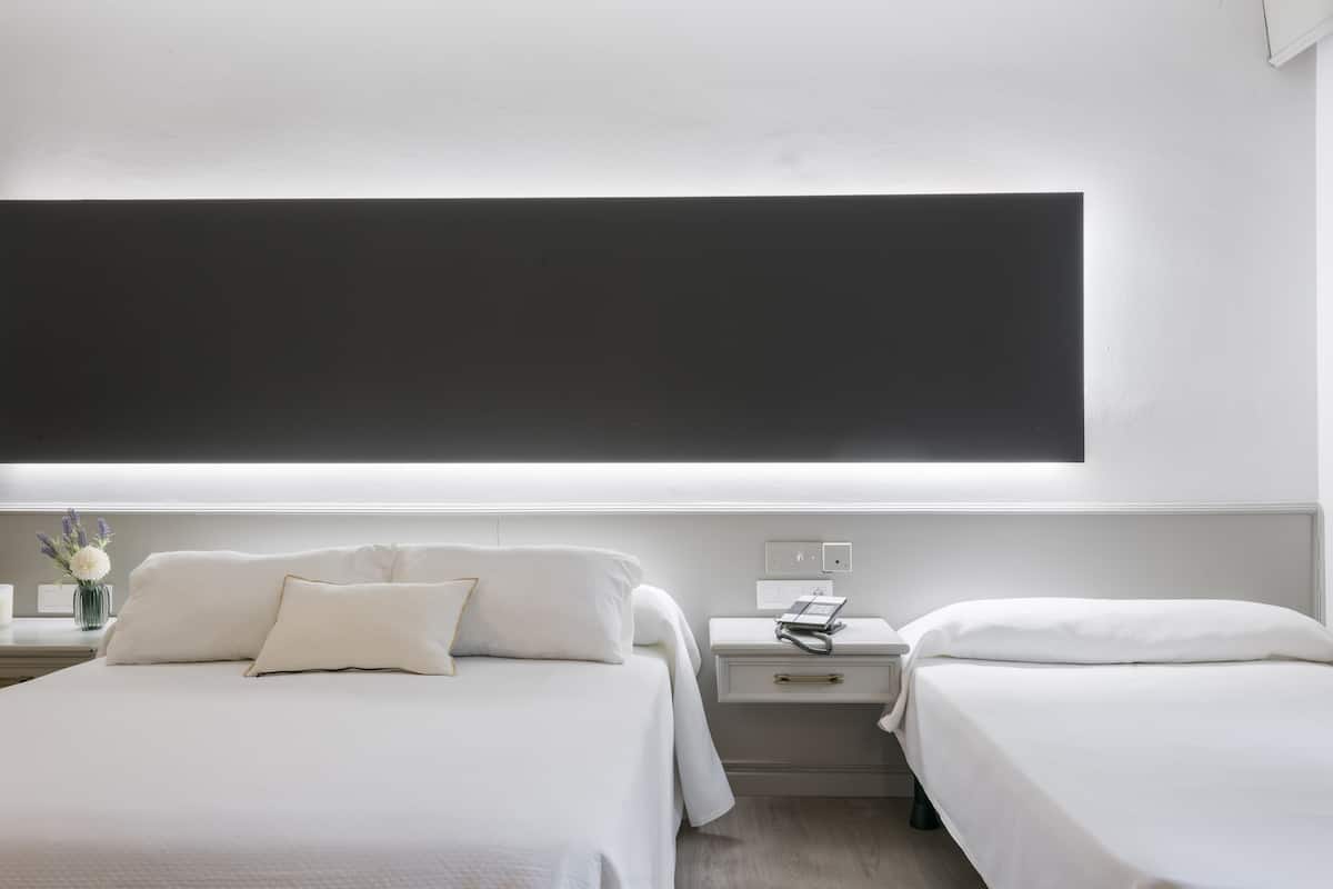 A modern hotel room with a large bed, bedside tables, a nightstand, and a wall-mounted light fixture.