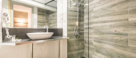 Un baño moderno con un espejo grande, un lavamanos blanco y una ducha con cerramiento de vidrio.