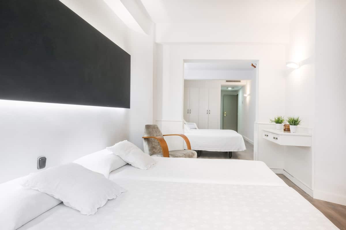 A modern hotel room with two beds, a chair, a desk, and a small plant.