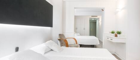 A modern hotel room with two beds, a chair, a desk, and a small plant.