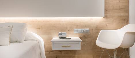 A modern bedroom with a wooden headboard, a bedside table with a lamp, a white chair, and a bed with white bedding.
