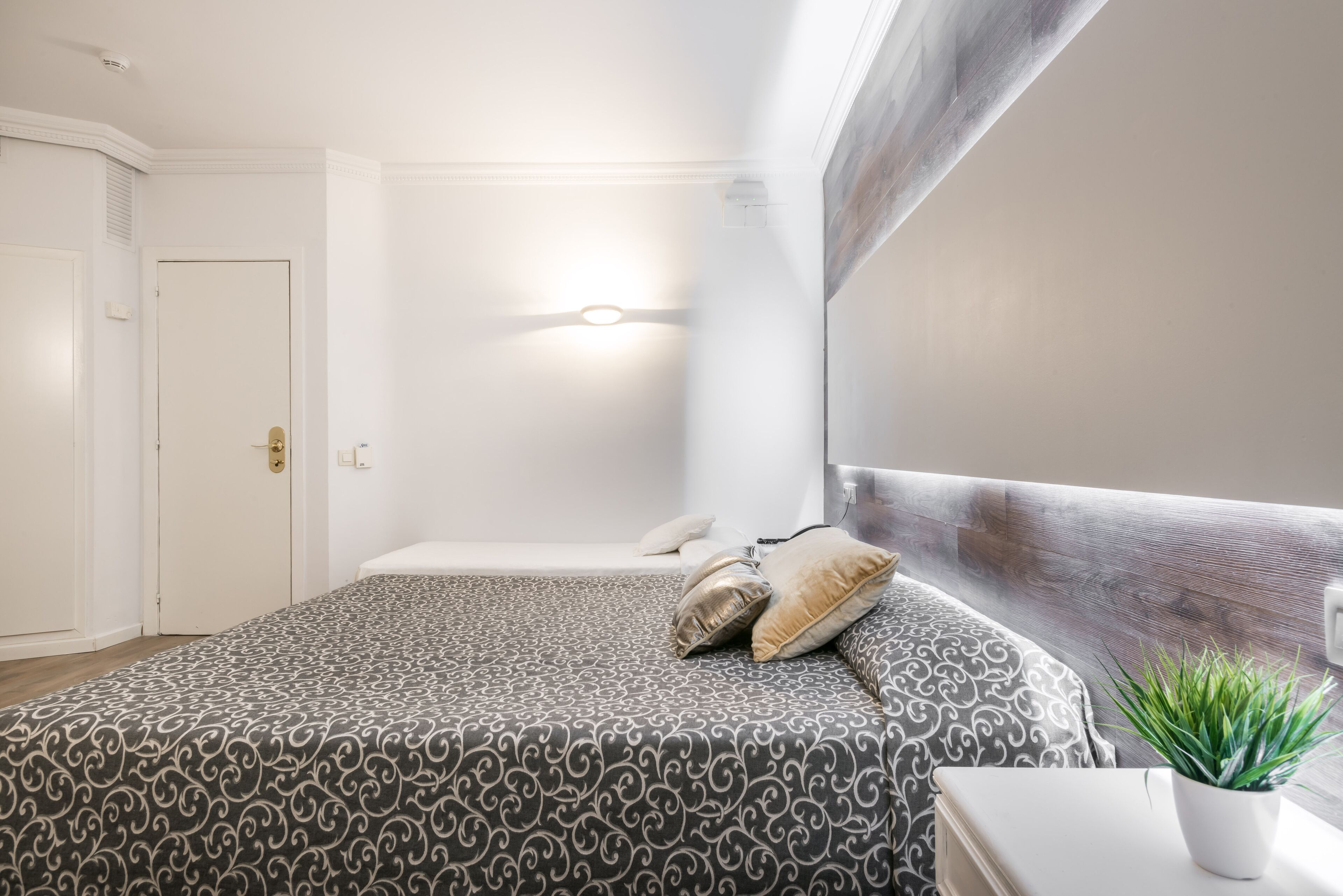Un dormitorio con una cama, una mesita de noche, una planta en maceta y una lámpara de pared.