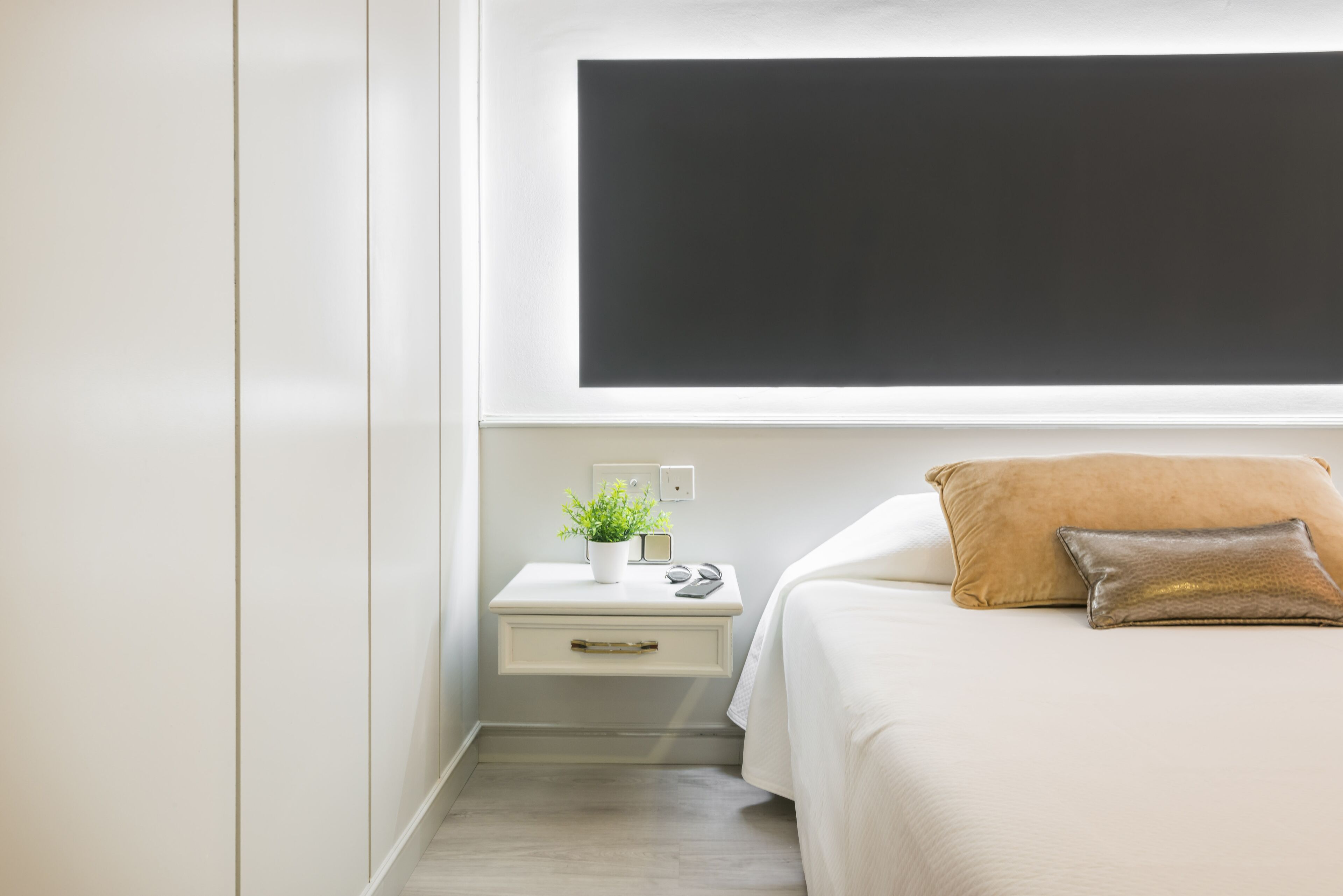 Un dormitorio con una cama, una mesita de noche, una planta en maceta y un televisor de pared.
