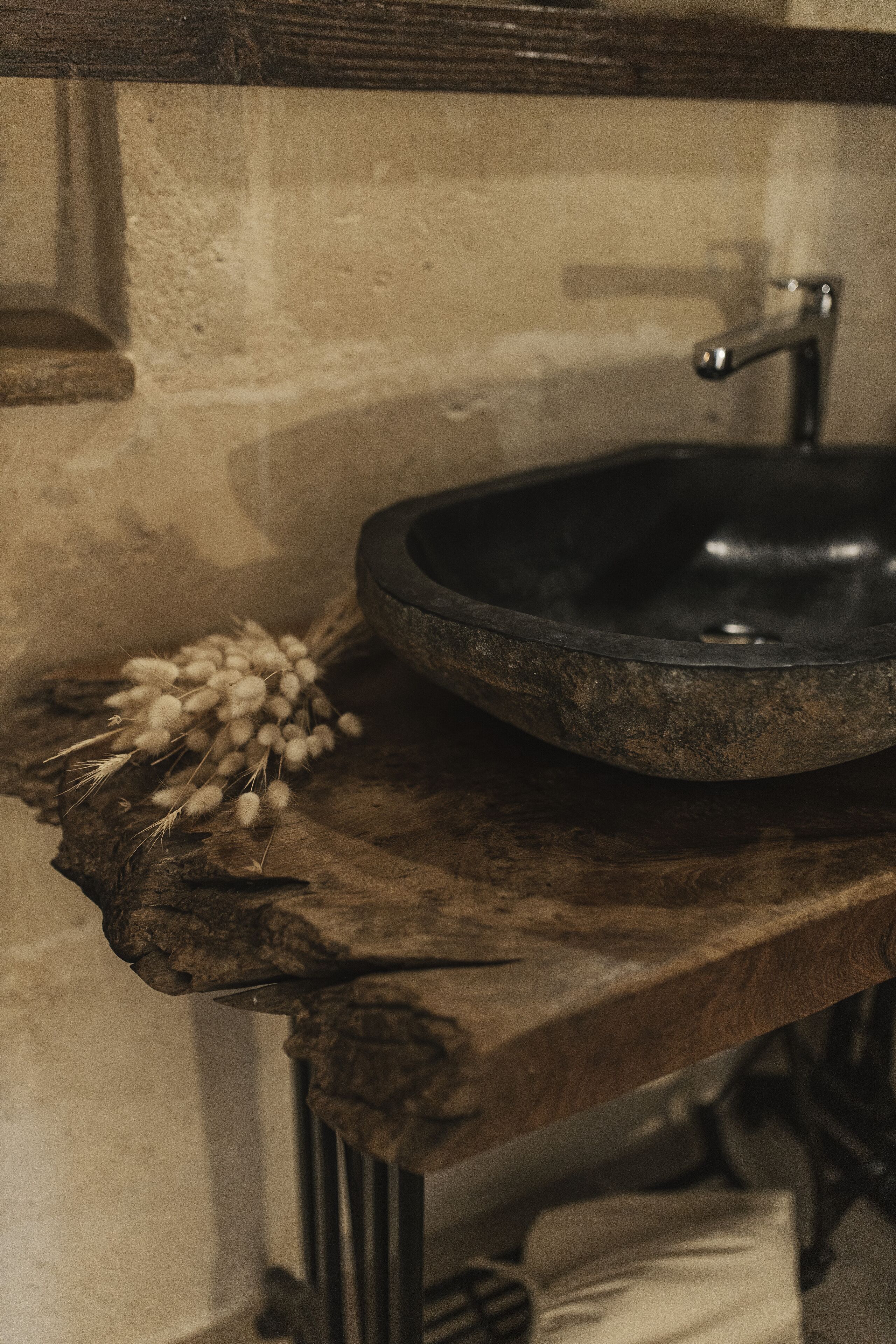 A rustic bathroom with a stone sink, wooden countertop, and a towel hanging on a metal rack.