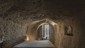 Een slaapkamer met een stenen plafond, een houten bed, een klein raam en een beeld aan de muur.