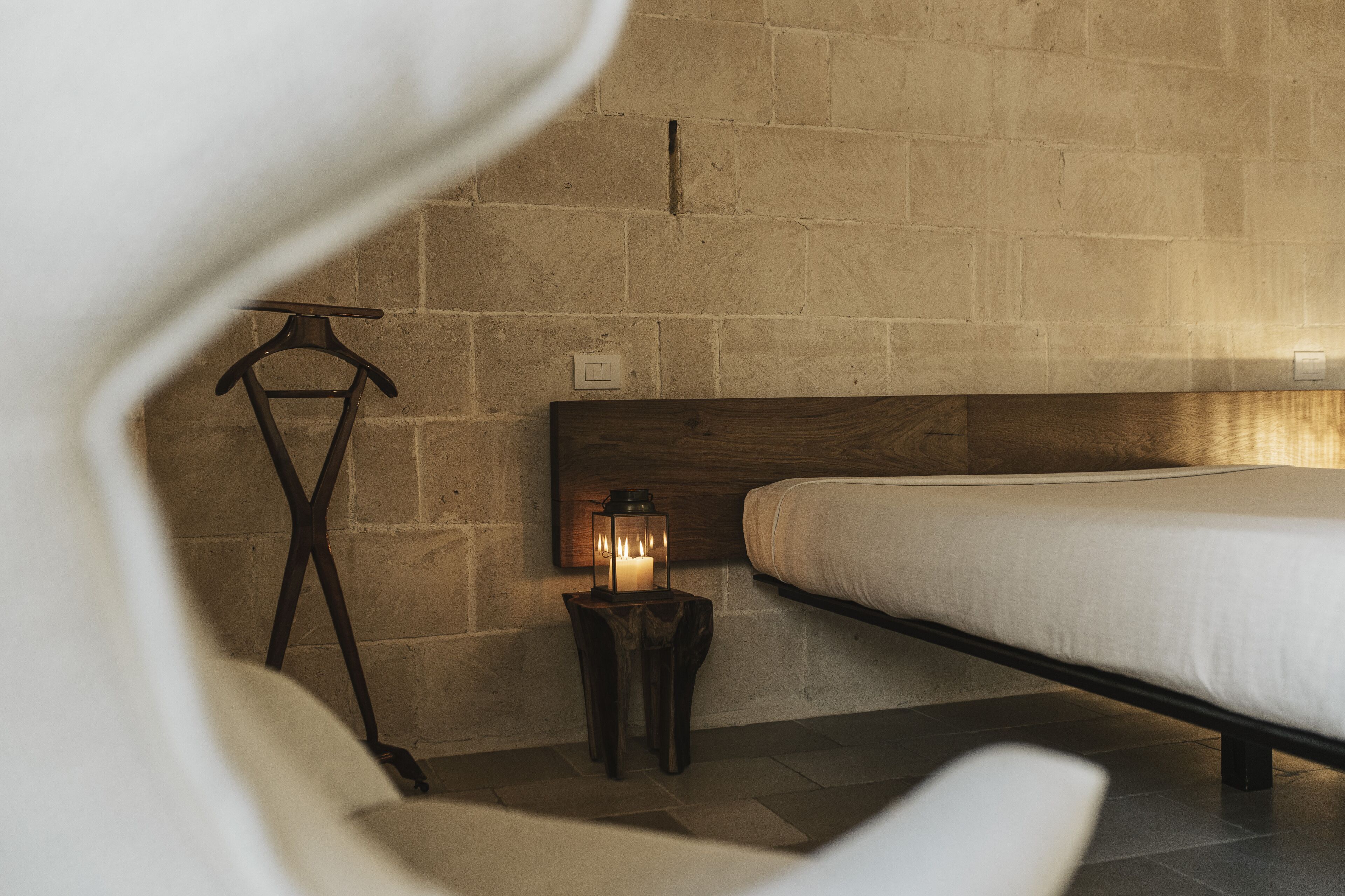 Un dormitorio con cabecera de madera, una mesita de noche con un farol y un perchero.
