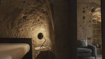 A room with a stone wall, a round table with a lamp, a bed, and a sofa.