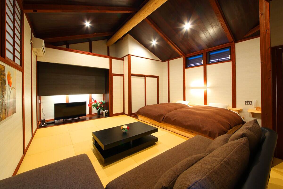 A traditional Japanese-style room with tatami flooring, a low table, a sofa, and a television.