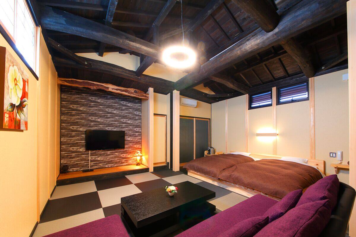 A modern living room with a checkered floor, a flat-screen TV mounted on a textured wall, a sofa, and a bed with a headboard.