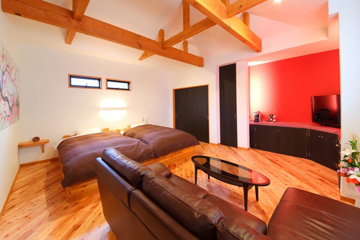 A living room with a sofa set, a coffee table, wooden beams on the ceiling, a TV, and a red accent wall.