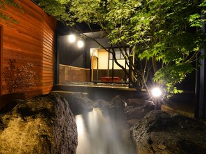 A traditional Japanese-style building with a wooden exterior, a stone pathway leading to a wooden entrance, and a small waterfall feature.