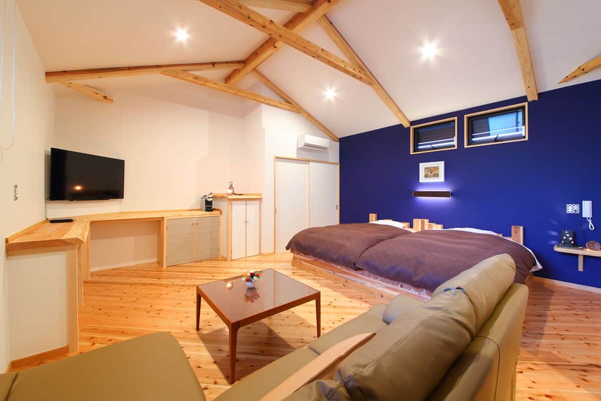 A room with a bed, a sofa, a TV, a small table, and a kitchenette.