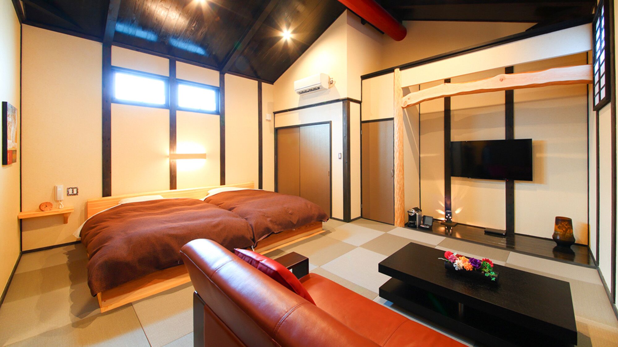 A hotel room with a bed, a sofa, a TV, a small table, and a wardrobe.