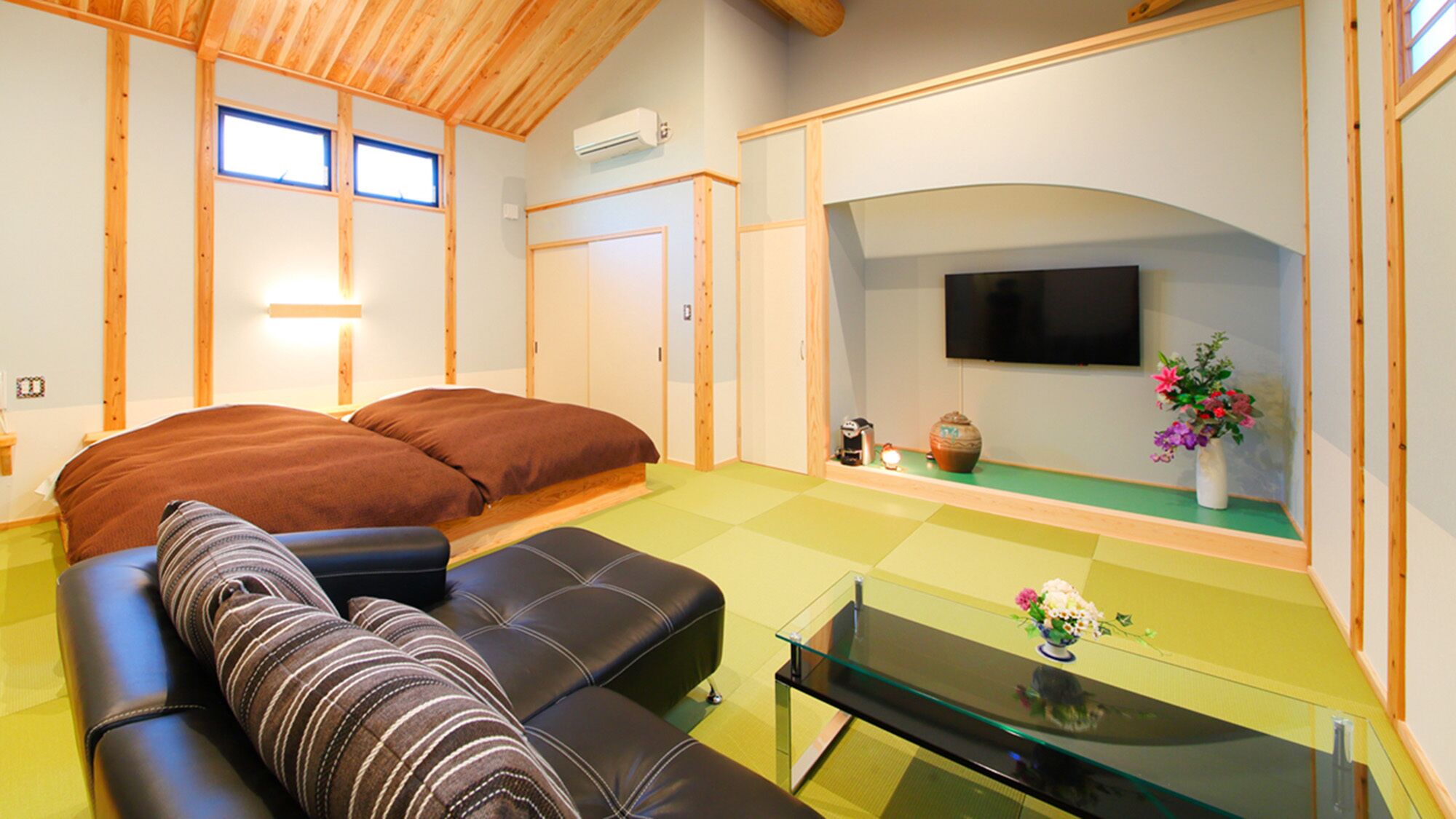 A room with a bed, a sofa, a TV, and a small table with flowers.