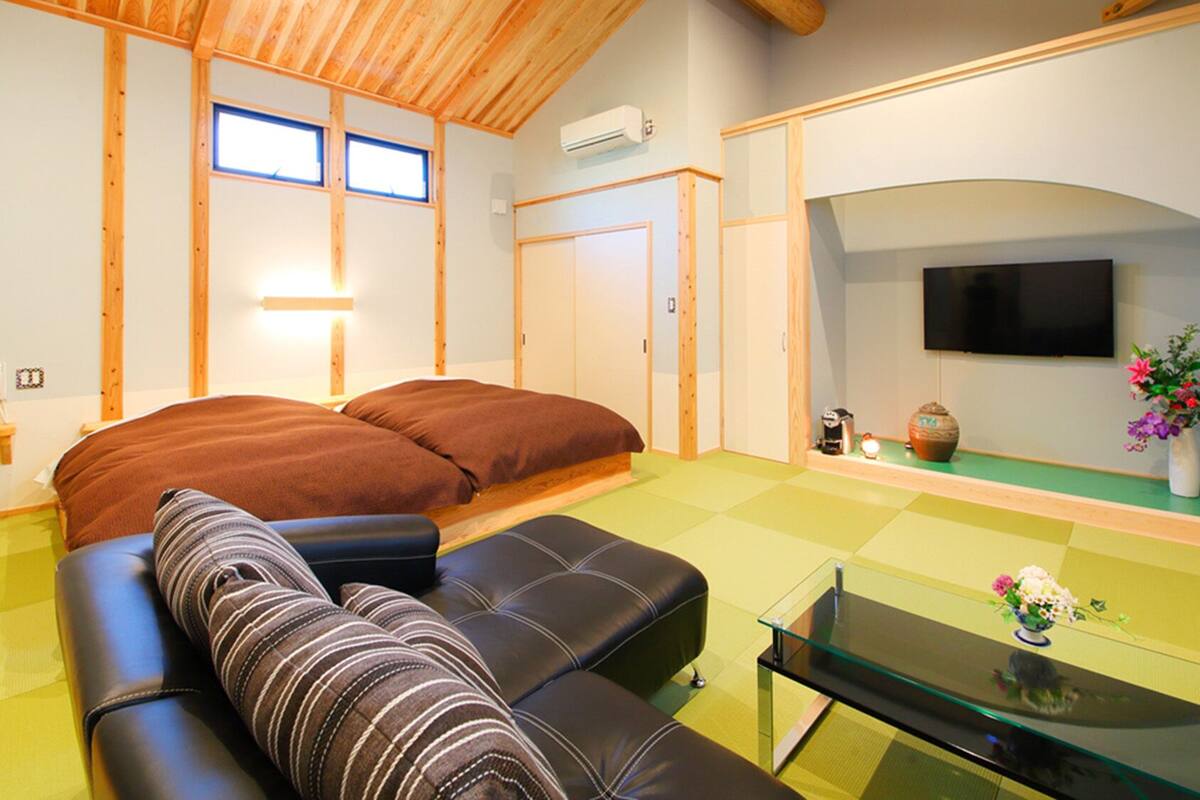 A room with a bed, a sofa, a TV, and a small table with flowers.