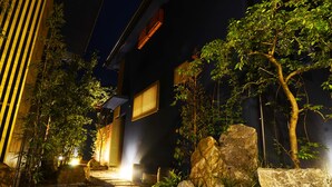 A nighttime garden pathway leading to a building with a dark facade and illuminated windows. - Shosei no Yado Shinan (Beppu)
