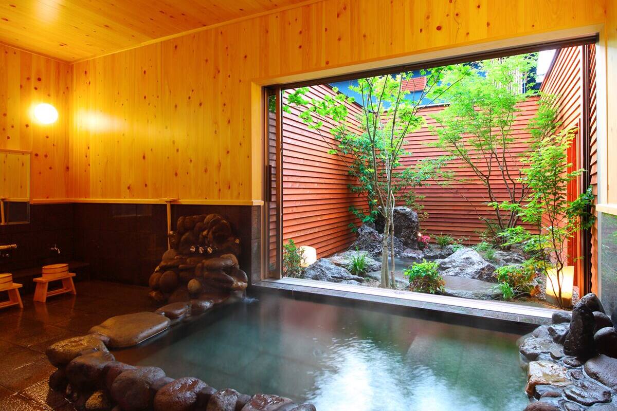 A wooden interior with a stone hot tub and a view of a red building outside.