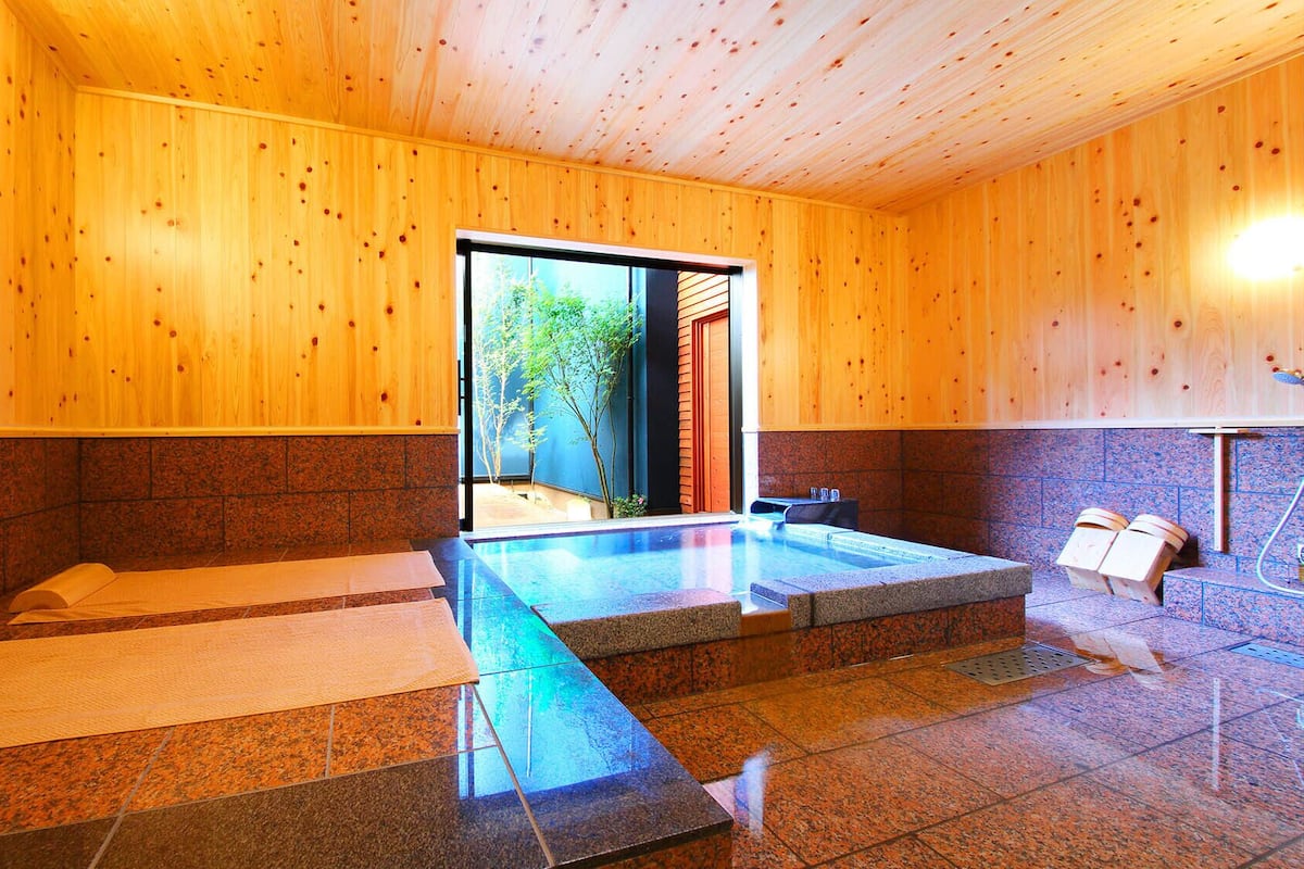 A wooden interior with a hot tub, stone flooring, and a view through a glass door.