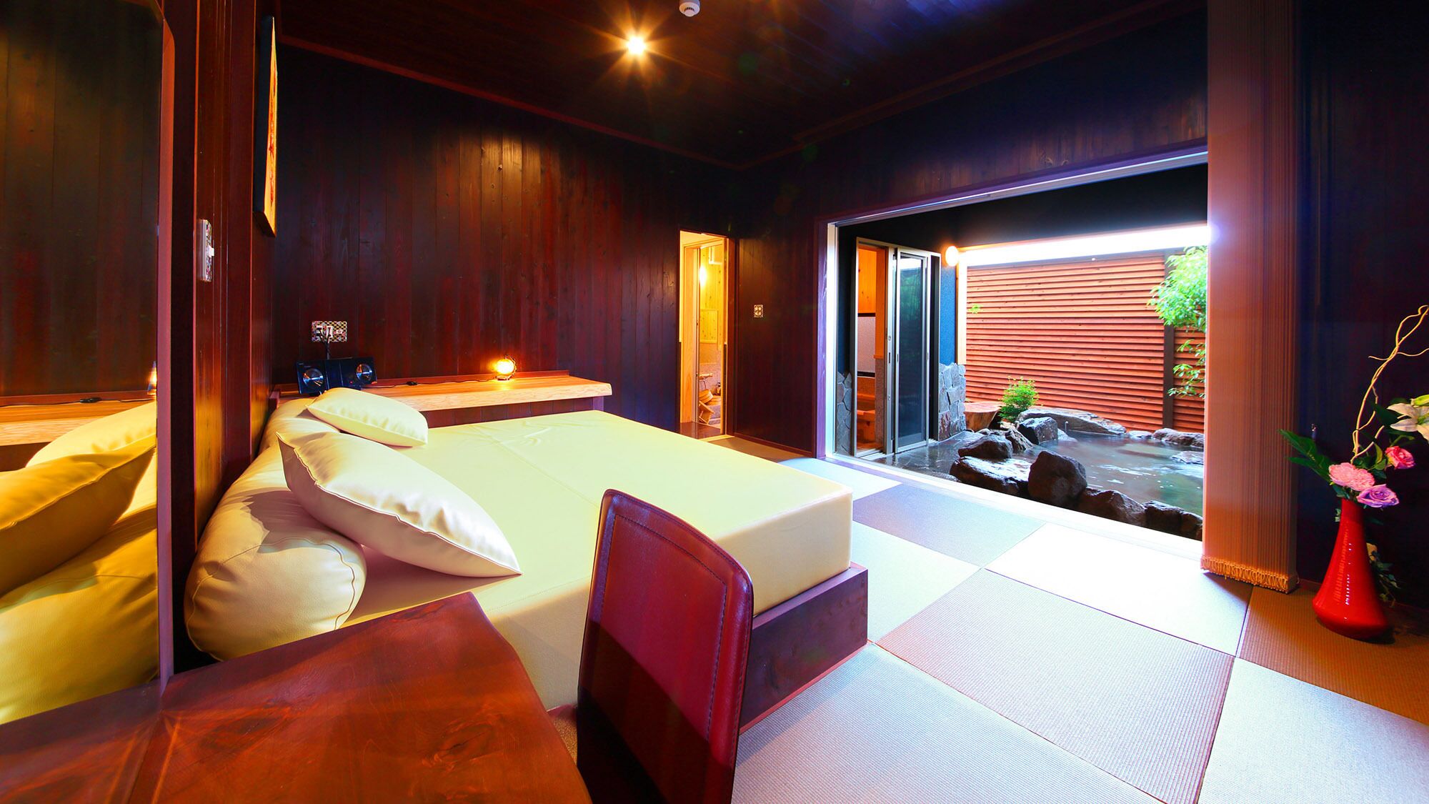 A bedroom with a bed, bedside table, and a view of a water feature outside.