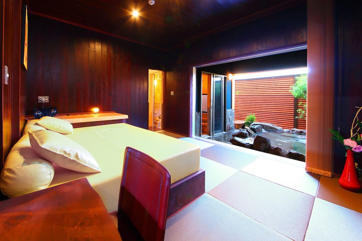 A bedroom with a bed, bedside table, and a view of a water feature outside.