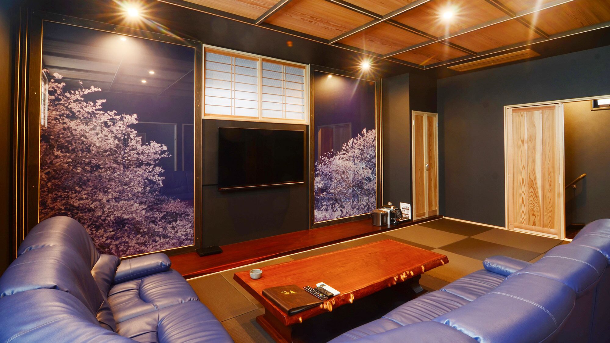 A room with a wooden ceiling, a TV mounted on the wall, a sofa, a coffee table, and a sliding door.