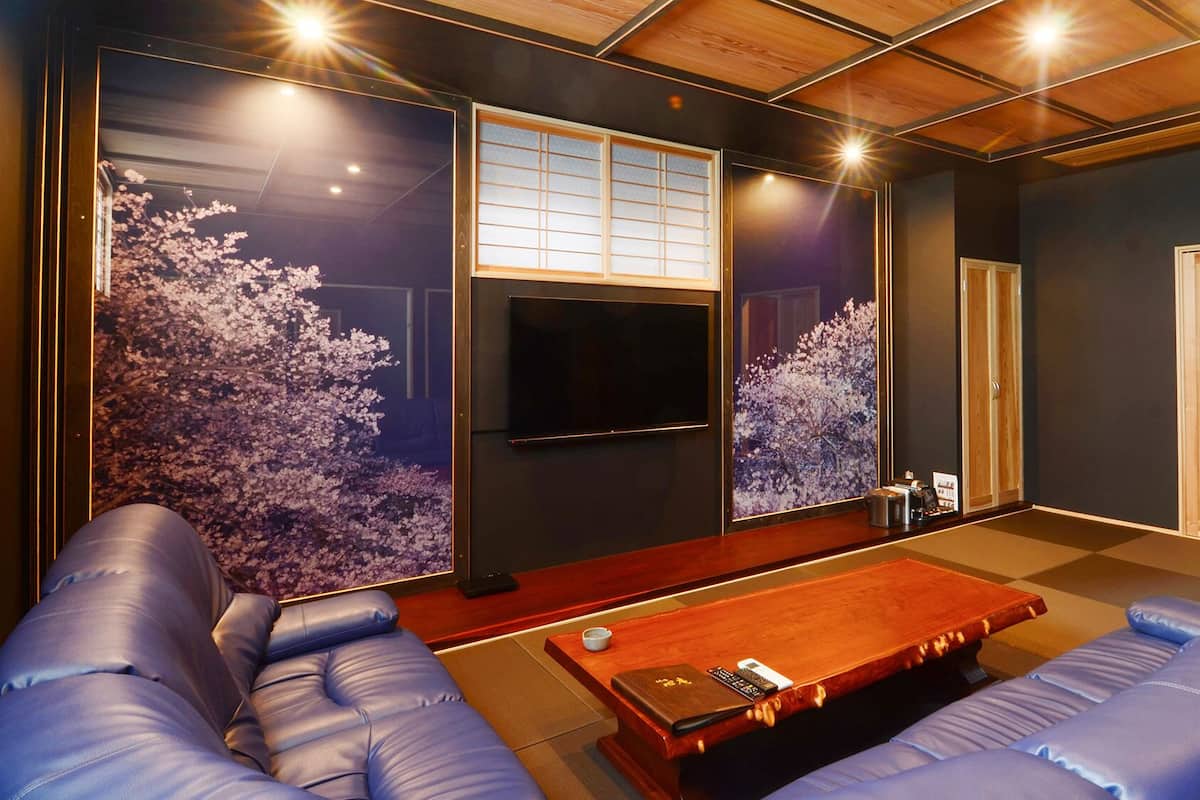 A room with a wooden ceiling, a TV mounted on the wall, a sofa, a coffee table, and a sliding door.