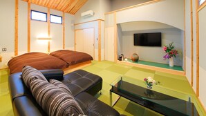 A room with a wooden ceiling, a bed, a sofa, a TV, and a small table with flowers. - Shosei no Yado Shinan (Beppu)