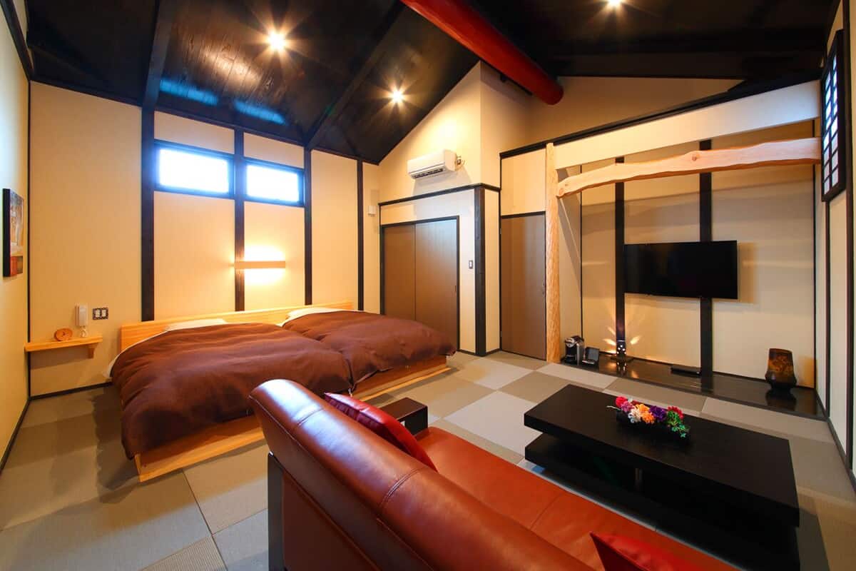 A modern hotel room with a bed, a sofa, a TV, and a small table with flowers.