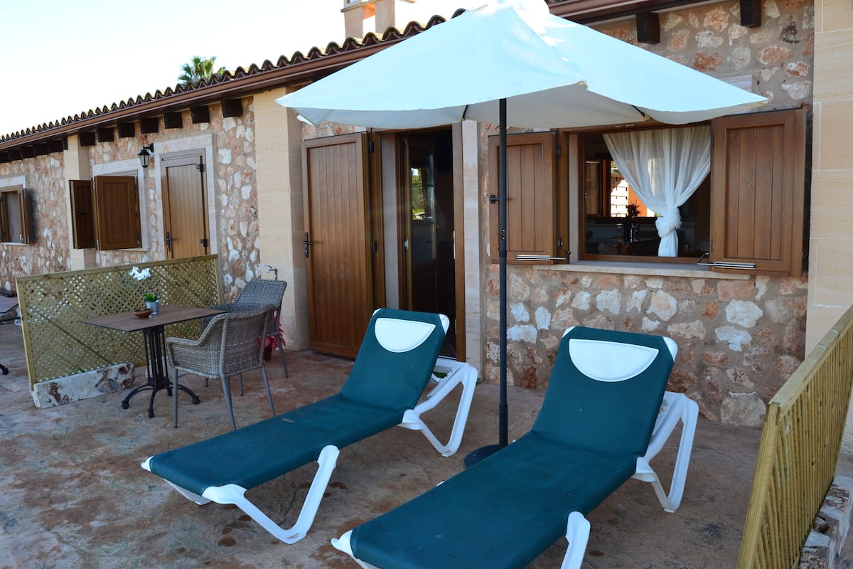 Un bâtiment en pierre avec deux fauteuils de jardin verts et une table avec des chaises à l’extérieur.