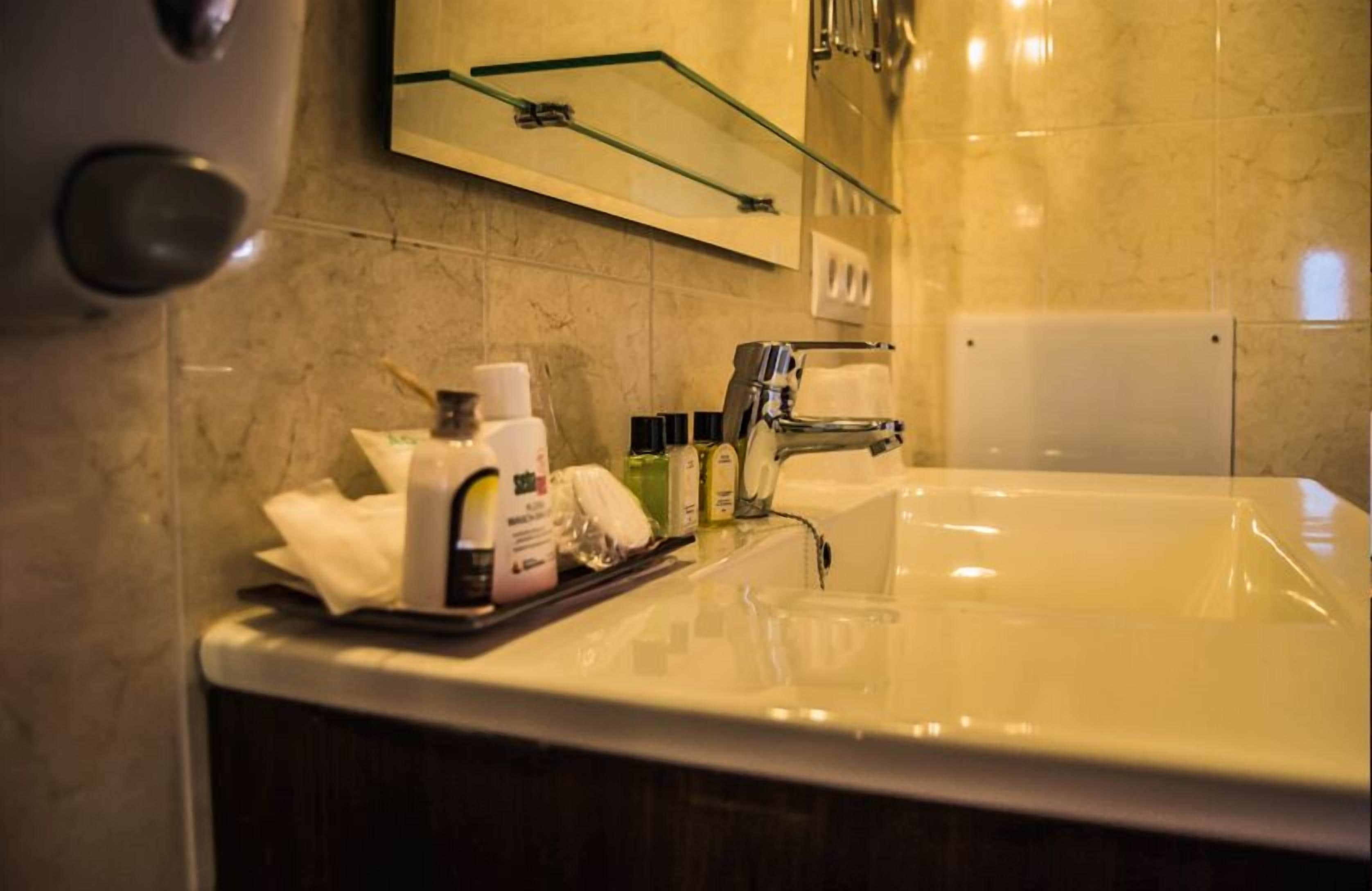 Une salle de bain avec un mur recouvert de carreaux de marbre, une étagère en verre au-dessus du lavabo et des articles de toilette posés sur le comptoir.