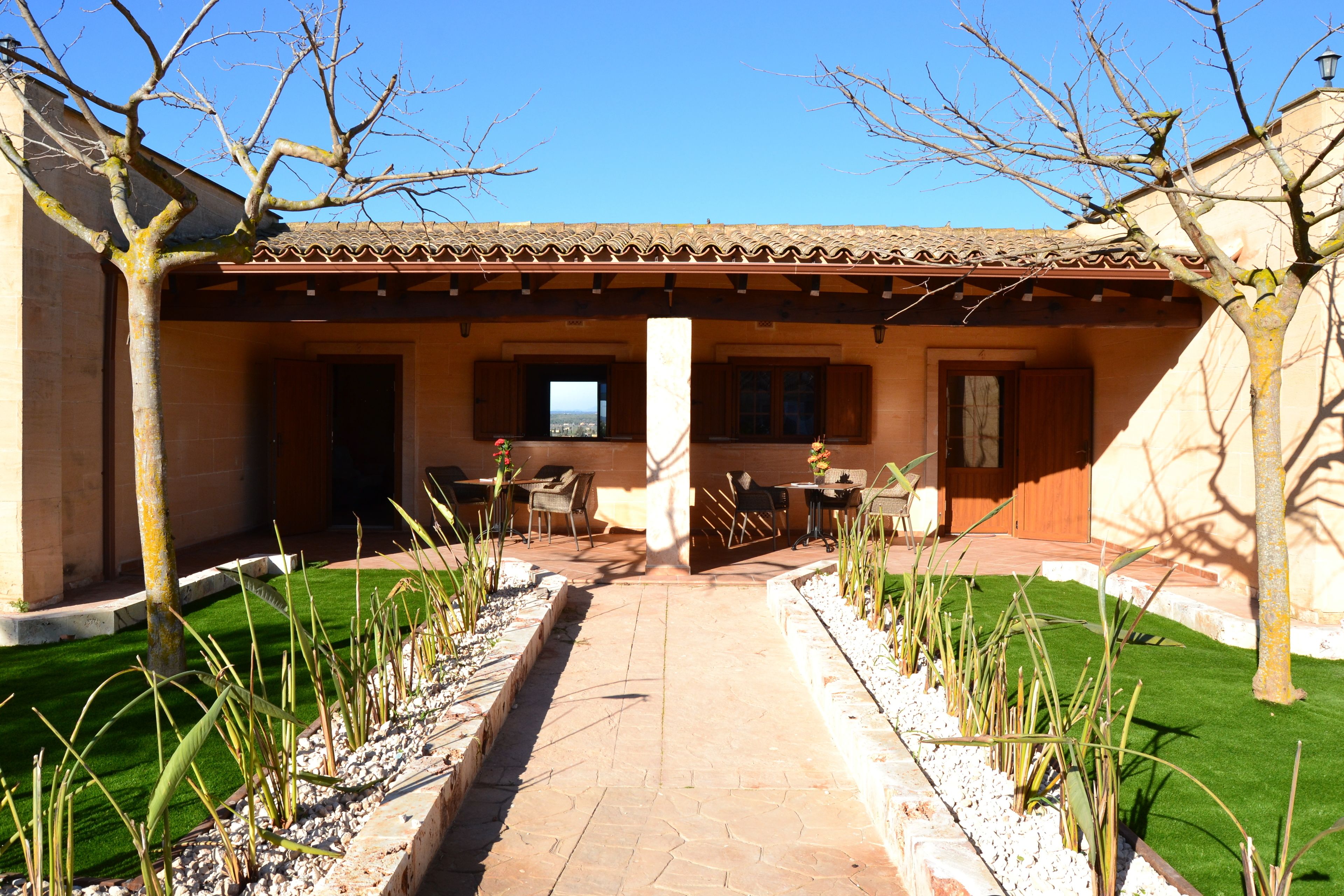 A courtyard with a tiled roof, a central column, and a pathway leading to a building entrance.