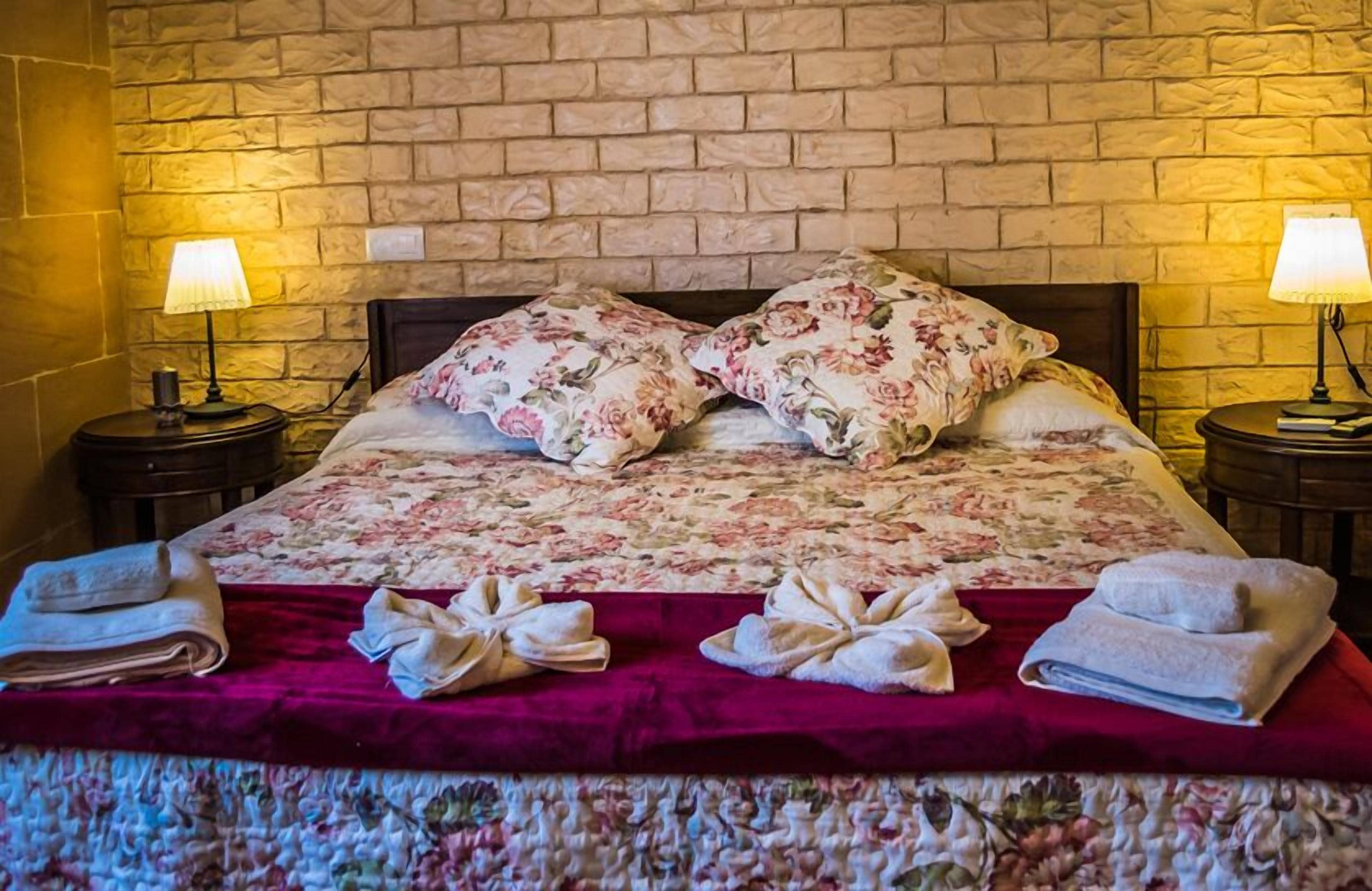 A neatly made bed with floral bedding, two bedside lamps, and towels on the bed.