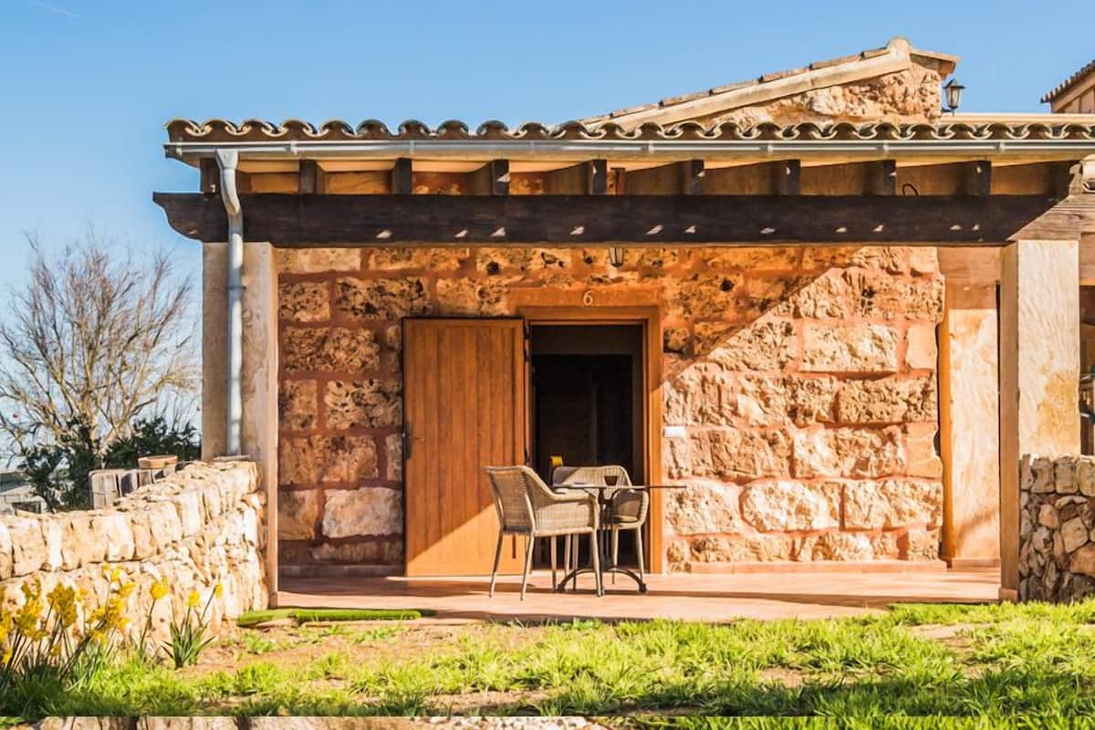 Un bâtiment en pierre avec une porte en bois et un patio couvert comprenant deux chaises.