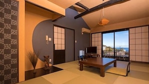 A traditional Japanese-style room with tatami flooring, a low table, a television, and a sliding door leading to a balcony with a view. - Ayunokaze (Ito)