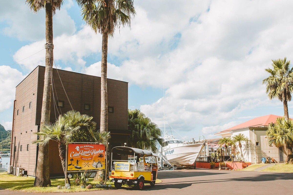 A tuk-tuk parked in front of a building with a sign for 'Calm Lanai Harbor & the Sea Station'.