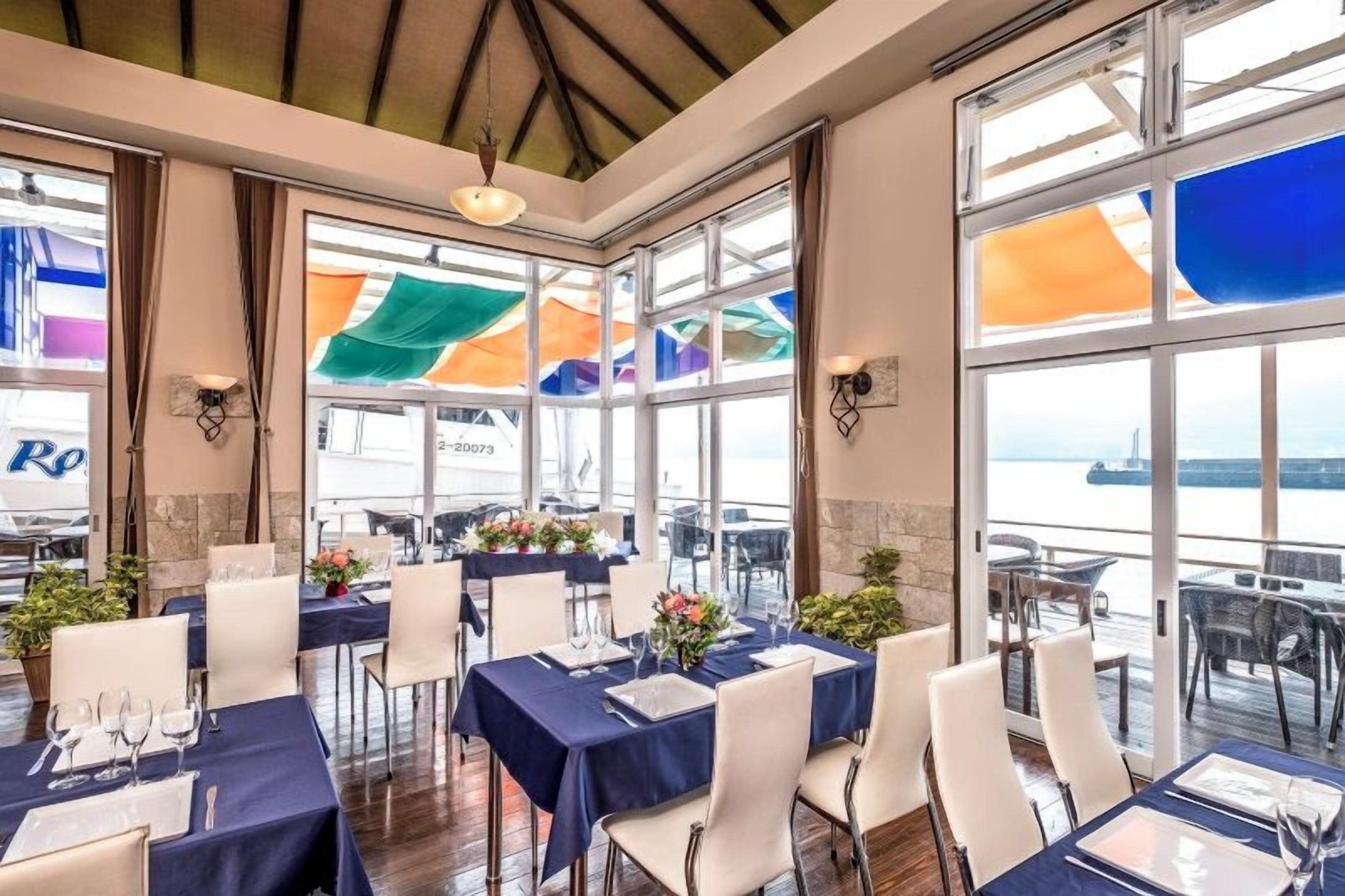 Ein Restaurant mit gedeckten Tischen, großen Fenstern und Blick auf das Wasser.